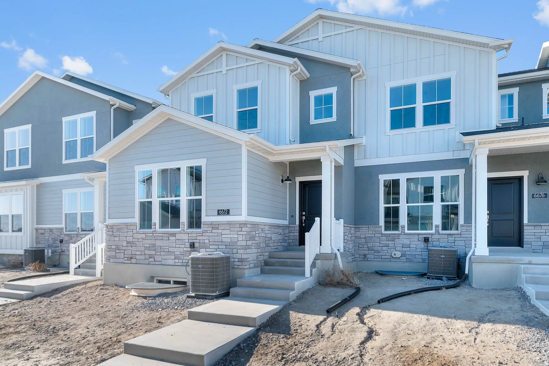 Multi-level façade featuring light gray siding, gray stucco, and stacked stone accents