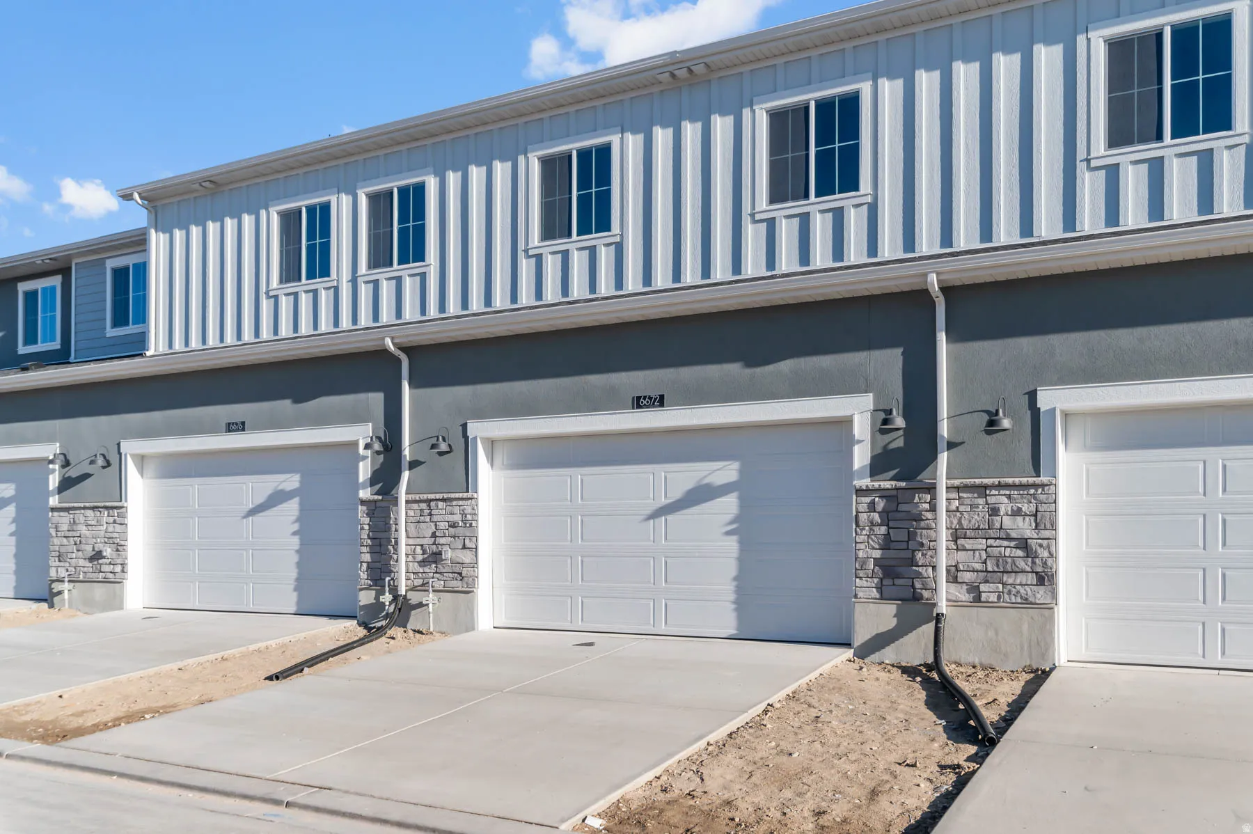 Multi-story exterior featuring a smooth stucco finish, vertical panel siding, and stone accents
