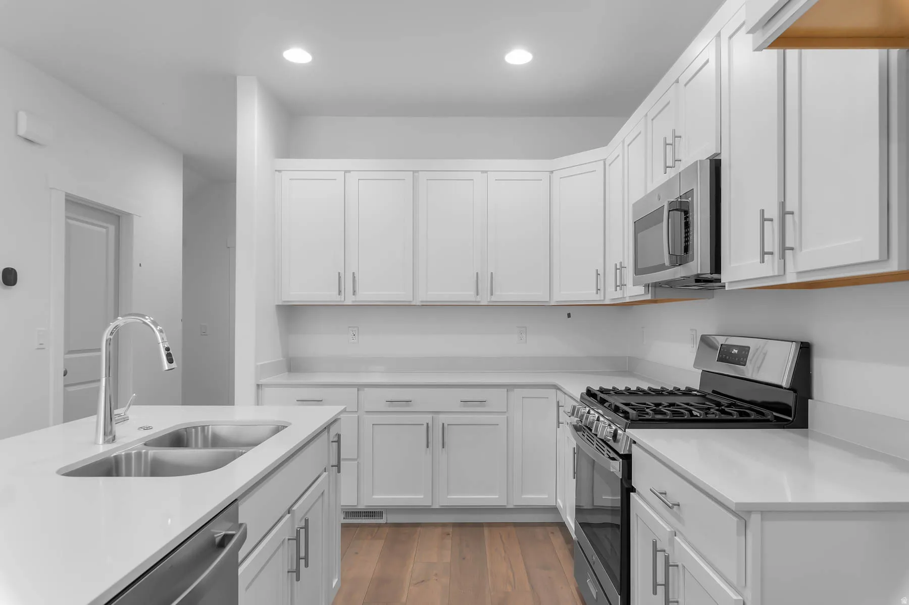 White shaker cabinetry, stainless steel appliances, dual basin sink, wood-finish flooring, and recessed lighting