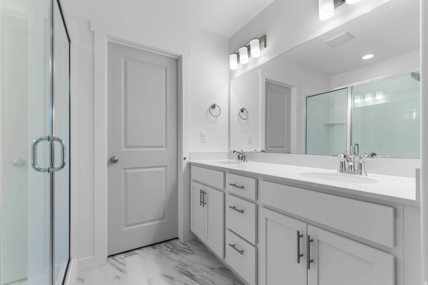 Dual vanity with white cabinetry and chrome hardware, white solid-surface countertops, and a full-width mirror