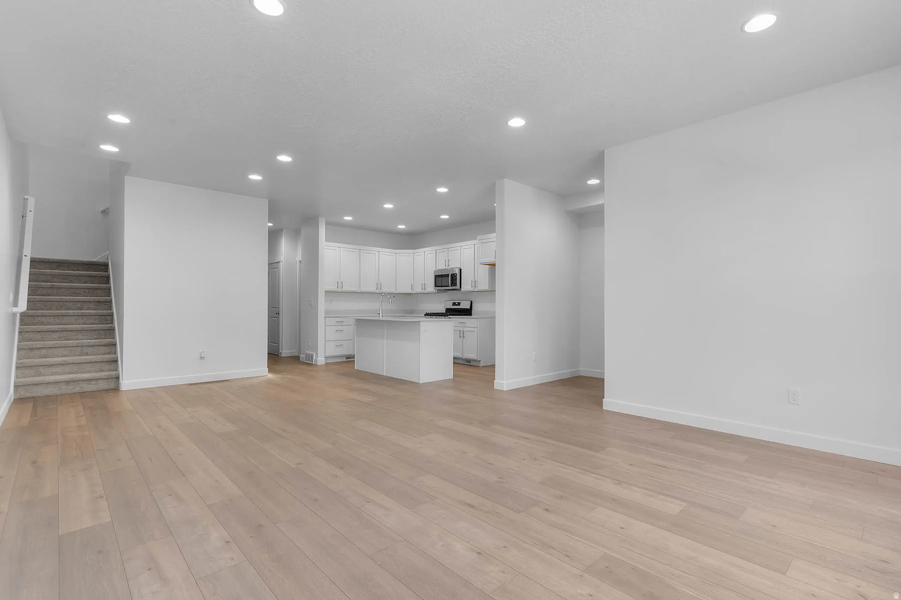 Recessed lighting, wood-finish flooring, white cabinetry, stainless steel appliances, and a central kitchen island