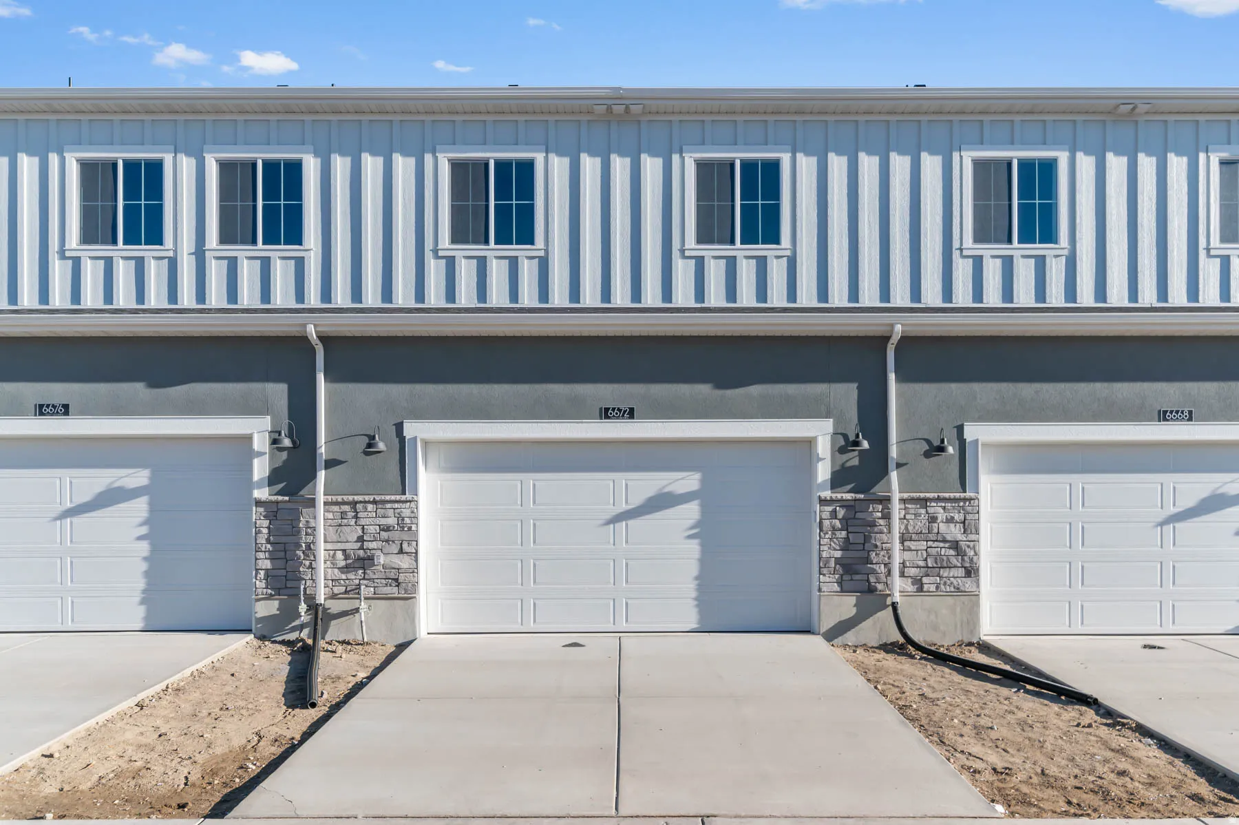 Vertical siding with multiple windows, stucco exterior, stone veneer accents, and individual garage doors