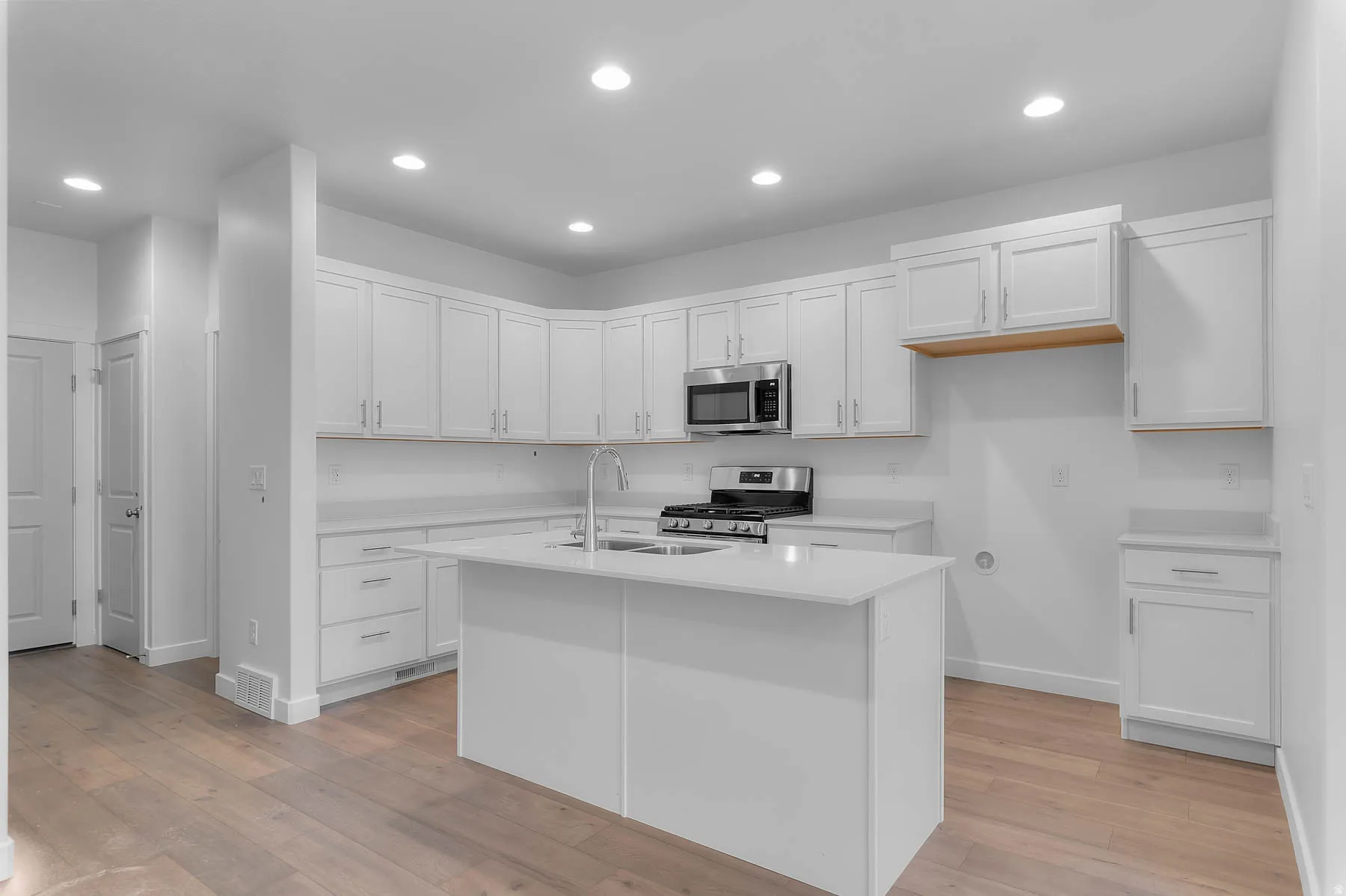 White shaker cabinetry, stainless steel appliances, central island with sink, recessed lighting, and wood-finish flooring