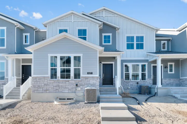 Multi-level facade with light-toned siding, white trim, and a prominent stone-finish base