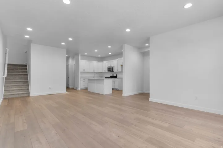 Recessed lighting, wood-finish flooring, white cabinetry, stainless steel appliances, and a central kitchen island