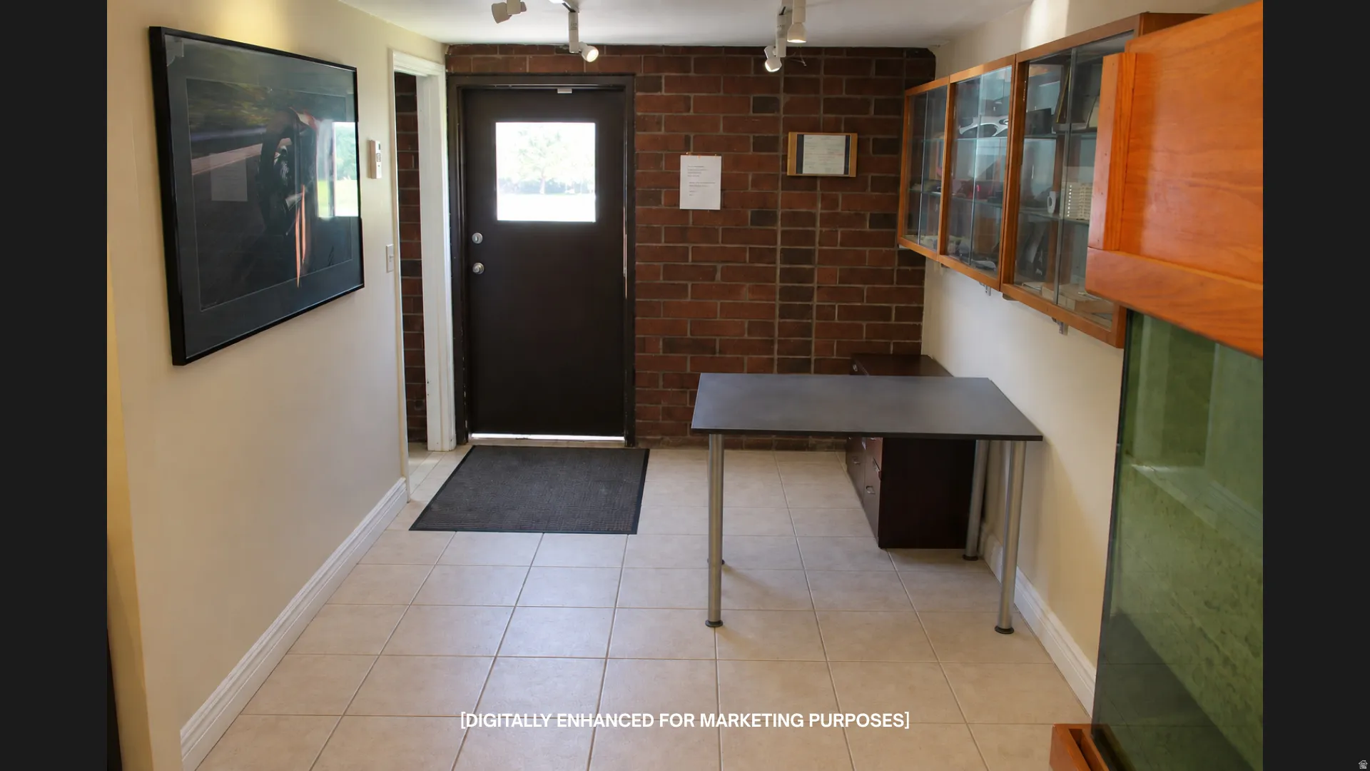 Tiled flooring, exposed brick wall, track lighting, built-in display cabinetry, and a door with an integrated window
