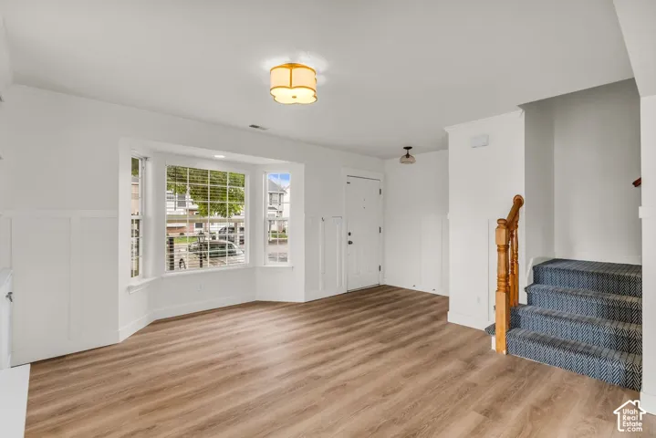 Interior space featuring wood-finish flooring, a three-panel bay window, white board-and-batten wall detailing, and a staircase with a wooden baluster railing