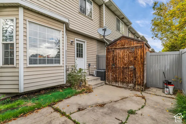 Exterior featuring horizontal siding, a bay window, concrete patio, and a detached wooden storage structure enclosed by perimeter fencing