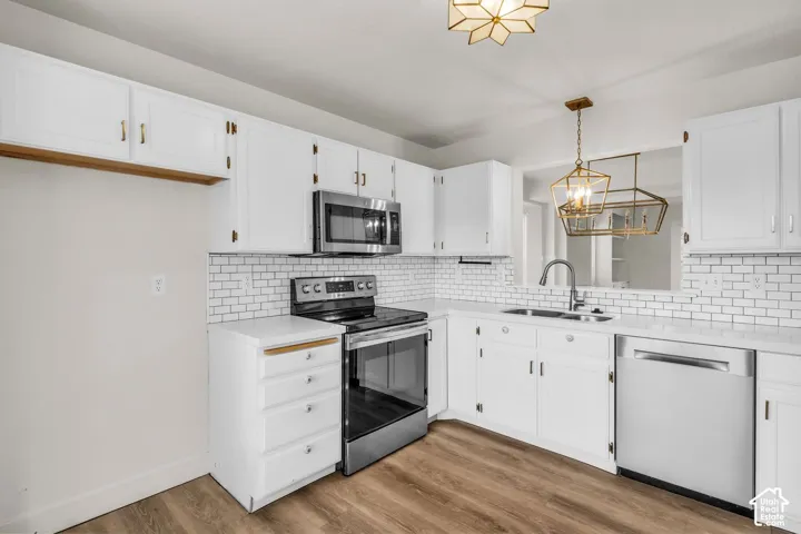 Kitchen featuring white cabinetry, subway tile backsplash, stainless steel appliances, wood-finish flooring, and geometric pendant lighting
