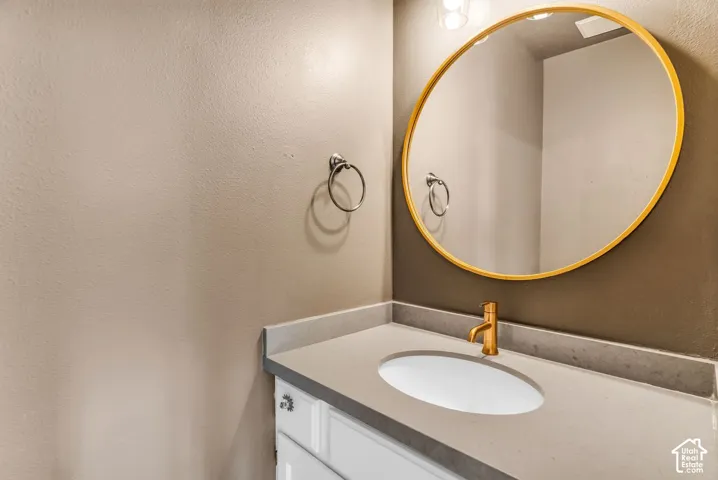 Vanity featuring a stone-composite countertop, undermount sink, brass-finish faucet, circular mirror with a metallic frame, and wall-mounted towel ring