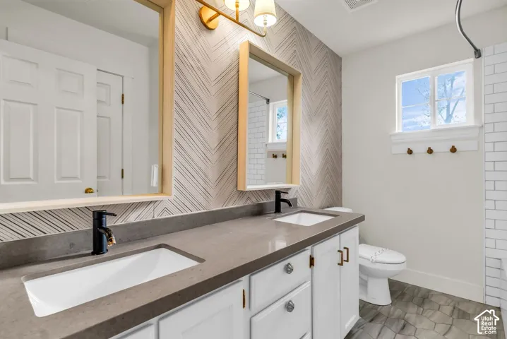 Double vanity featuring stone countertops, rectangular undermount sinks, matte black faucets, and chevron-patterned accent wall with framed mirrors