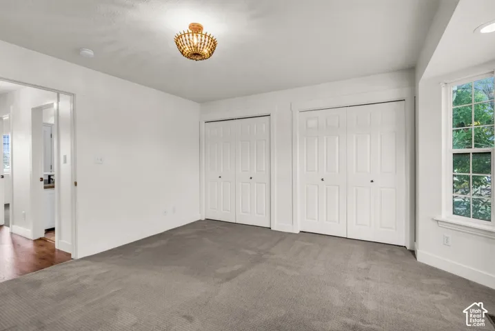 Neutral-toned carpeting, dual double-door closets with trim detailing, multi-pane bay window, and a decorative semi-flush mount fixture
