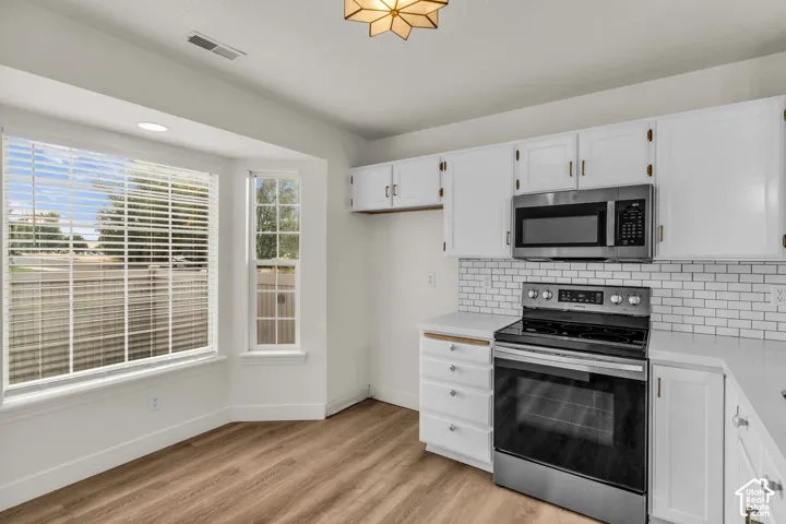 Kitchen featuring white cabinetry, subway tile backsplash, stainless steel appliances, wood-finish flooring, and a bay window