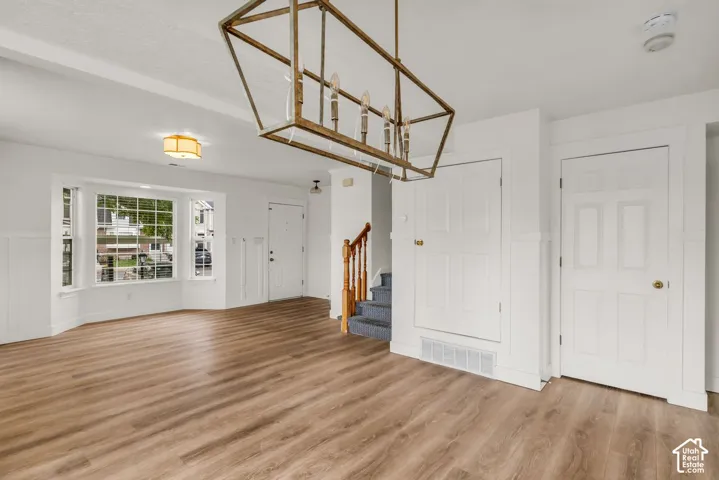 Open-concept interior featuring wood-finish flooring, a bay window, wainscoting, an industrial-style geometric chandelier, and a wood-railing staircase