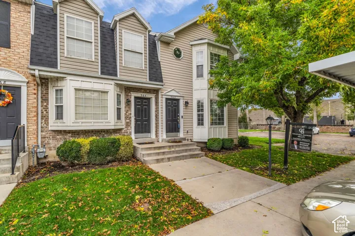 Multi-level exterior featuring light-toned horizontal siding, a mix of brick and dark shingle mansard-style roofing, bay windows, and concrete front stoops