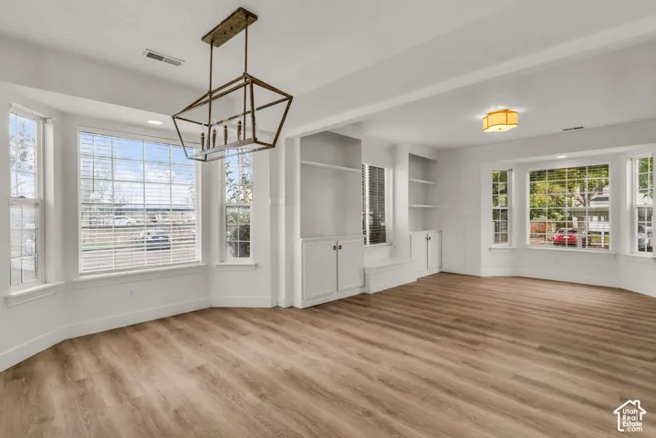 Open-concept space featuring wood-finish flooring, dual bay windows, custom built-in cabinetry with shelving, and a prominent geometric metal-frame chandelier