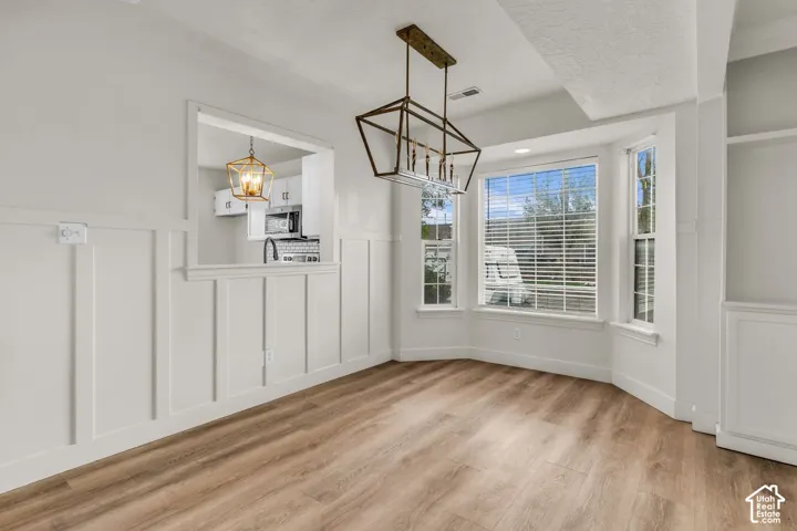 Dining space featuring wood-finish flooring, board-and-batten wall detailing, a bay window, and a geometric metal-frame chandelier