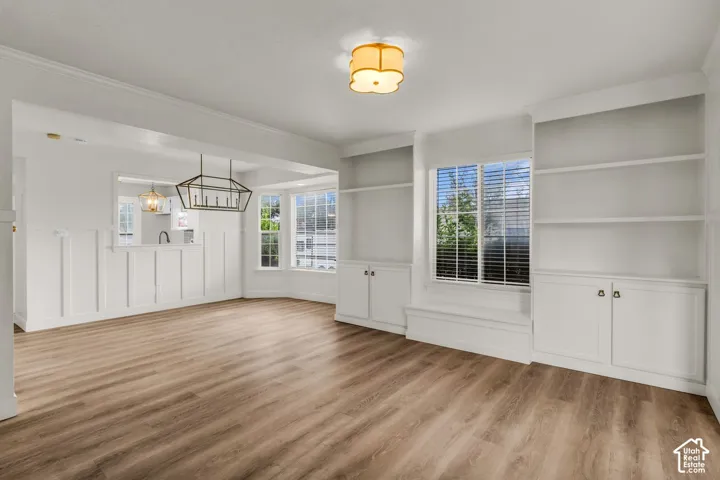 Wood-finish flooring, white board-and-batten wall paneling, floor-to-ceiling built-in cabinetry, bay window, and a geometric metal chandelier