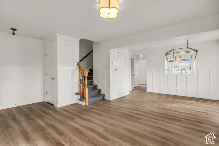 Interior space featuring white board-and-batten wainscoting, wood-finish flooring, a geometric metal chandelier, and a wood-railing staircase with carpeted treads