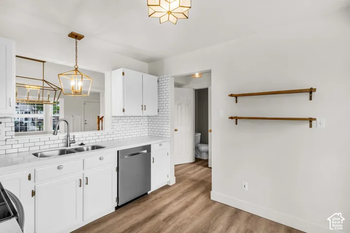 Kitchen featuring white cabinetry, subway tile backsplash, stainless steel dishwasher, wood-finish flooring, and geometric pendant lighting
