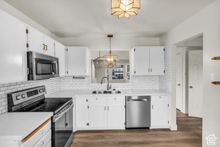 Kitchen featuring white cabinetry, subway tile backsplash, stainless steel appliances, wood-finish flooring, and metallic geometric pendant lighting