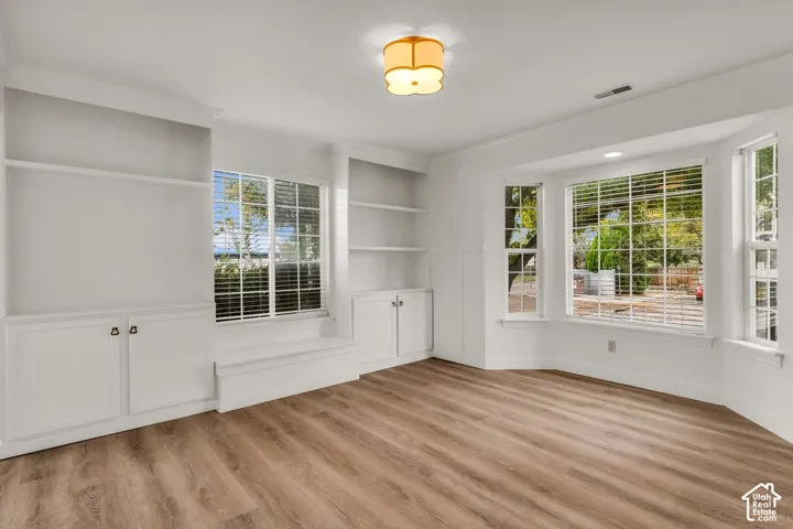 Interior featuring wood-finish flooring, built-in cabinetry with shelving, a window seat, and a bay window configuration