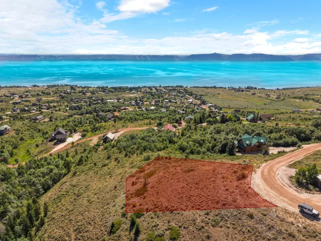 Expansive lot with partial tree coverage, adjacent to a dirt road, offering distant water and mountain scenery