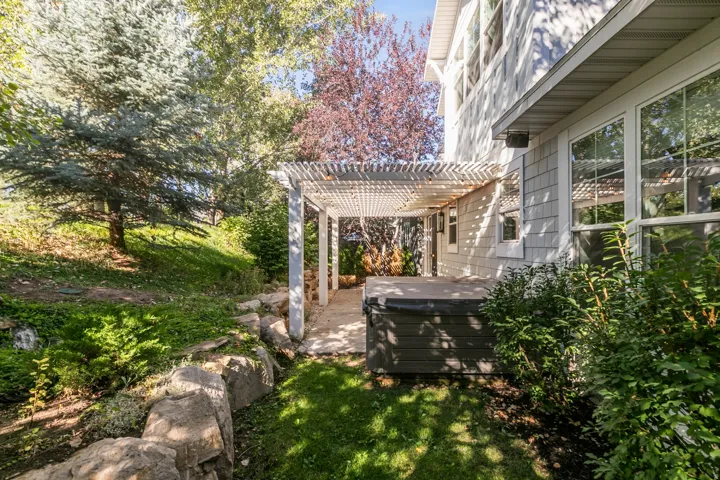Lattice pergola structure with concrete patio, integrated spa, and shingle siding