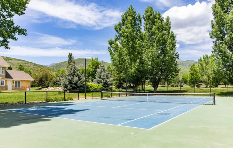 Private tennis court with a blue playing surface, surrounded by mature trees and mountain scenery