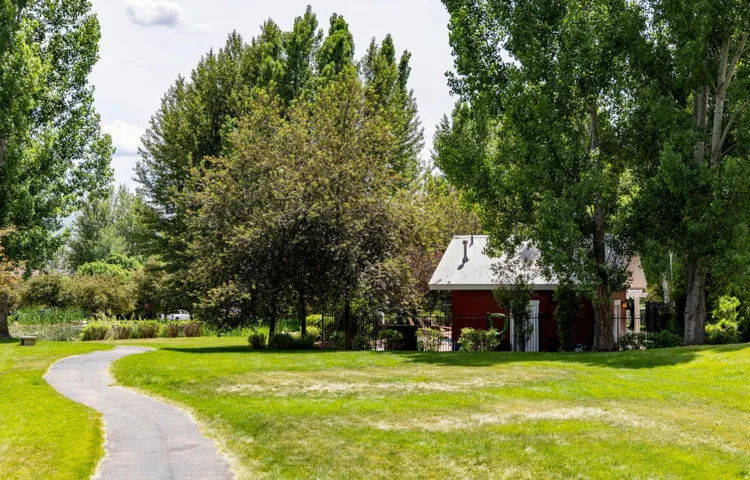 Manicured lawn, mature trees, winding paved pathway, red exterior structure, and a white roof
