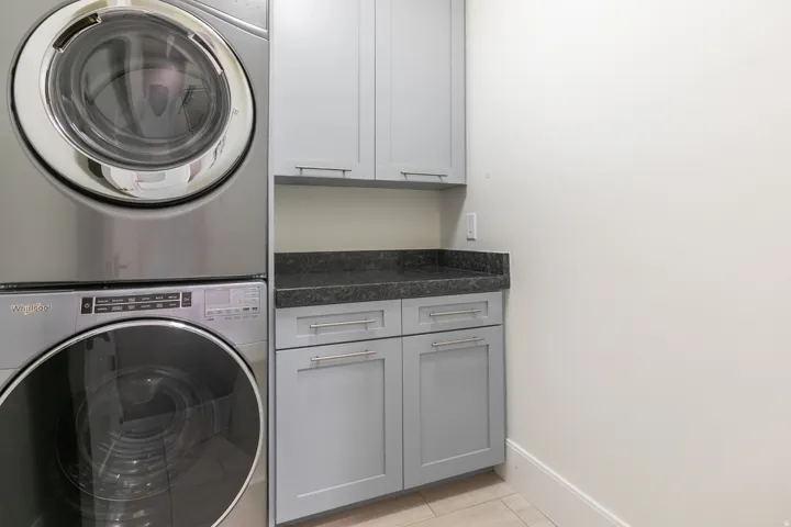 Stacked washer and dryer, light gray cabinetry, dark countertop, and tiled flooring