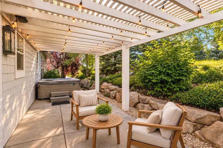 Covered patio with a built-in hot tub, concrete flooring, and surrounding landscaping with rock accents