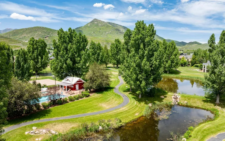 Scenic landscape featuring lush green hills, multiple ponds, mature trees, a swimming pool, and a red cabana with an attached covered patio