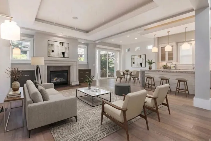 Open-concept living area featuring wood-finish flooring, a tray ceiling, and a fireplace with a stone surround