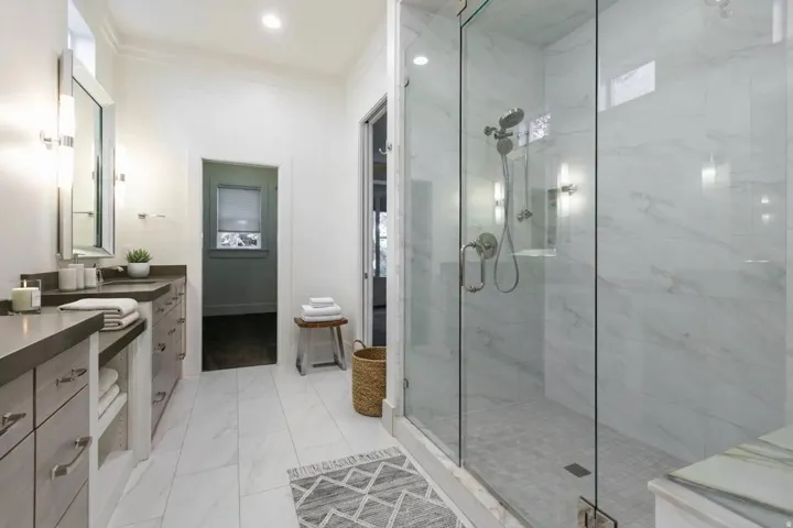 Dual vanity with undermount sinks, frameless glass shower enclosure, large format tile flooring, and custom cabinetry with contemporary hardware