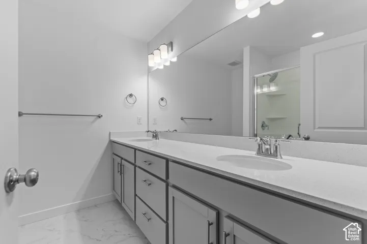 Dual-sink vanity with light gray shaker cabinetry, engineered stone countertops, undermount sinks, and chrome fixtures, complemented by full-width vanity mirrors and stone-finish flooring