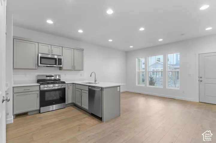 Kitchen featuring grey cabinetry, white countertops, stainless steel appliances, and wood-finish flooring with recessed lighting