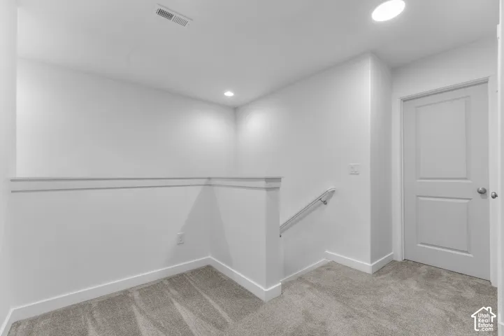 Neutral-toned carpet, recessed lighting, solid-core interior door, and minimalist wall partition with metal handrail