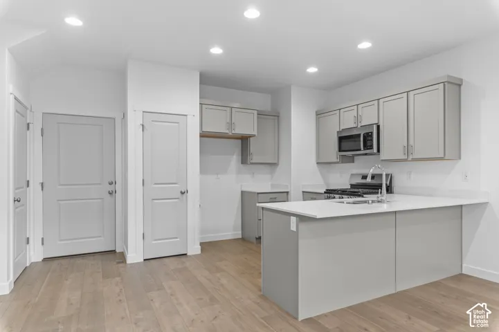 Kitchen featuring light-toned cabinetry, solid-surface countertops, recessed ceiling lighting, stainless steel built-in microwave, and wood-finish flooring