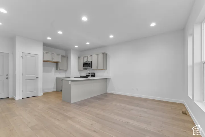 Kitchen area featuring light-toned cabinetry, quartz countertops, a central island, recessed lighting, and wood-finish flooring