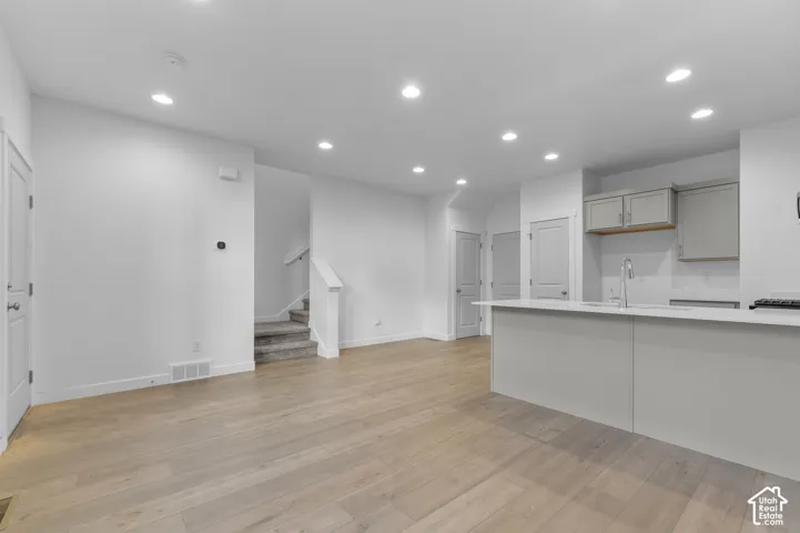 Open interior featuring recessed lighting, wood-finish flooring, and a kitchen island with a dual-basin stainless steel sink