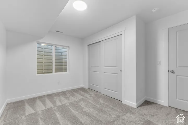 Neutral-toned carpeted flooring, sliding closet doors, flush-mount lighting, and egress window with corrugated steel window well