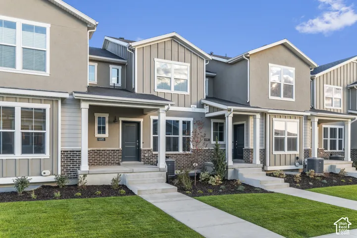 Multi-family exterior featuring a mixed-material facade of vertical siding and brick masonry, covered front porches with square columns, and concrete walkways