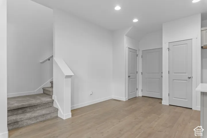 Neutral-toned interior featuring wood-finish flooring, recessed lighting, carpeted stairs with a white handrail, and shaker-style interior doors