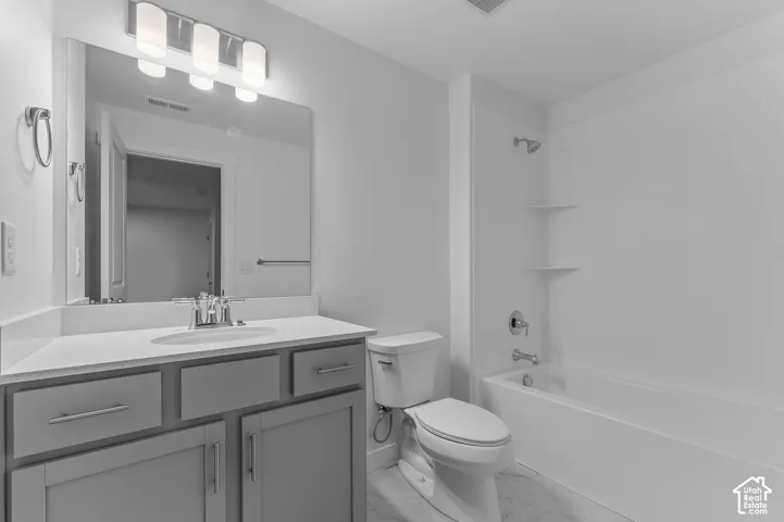 Bathroom featuring a grey vanity with a light-toned solid surface countertop, an undermount sink with a polished chrome faucet, a large wall-mounted mirror, four-light vanity fixture, and a tub-shower combination