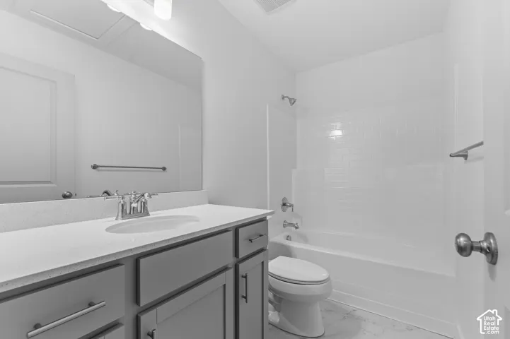 Bathroom featuring a gray vanity with a stone-finish countertop, undermount sink, a large wall-mounted mirror, and a shower-tub combination with subway tile surround