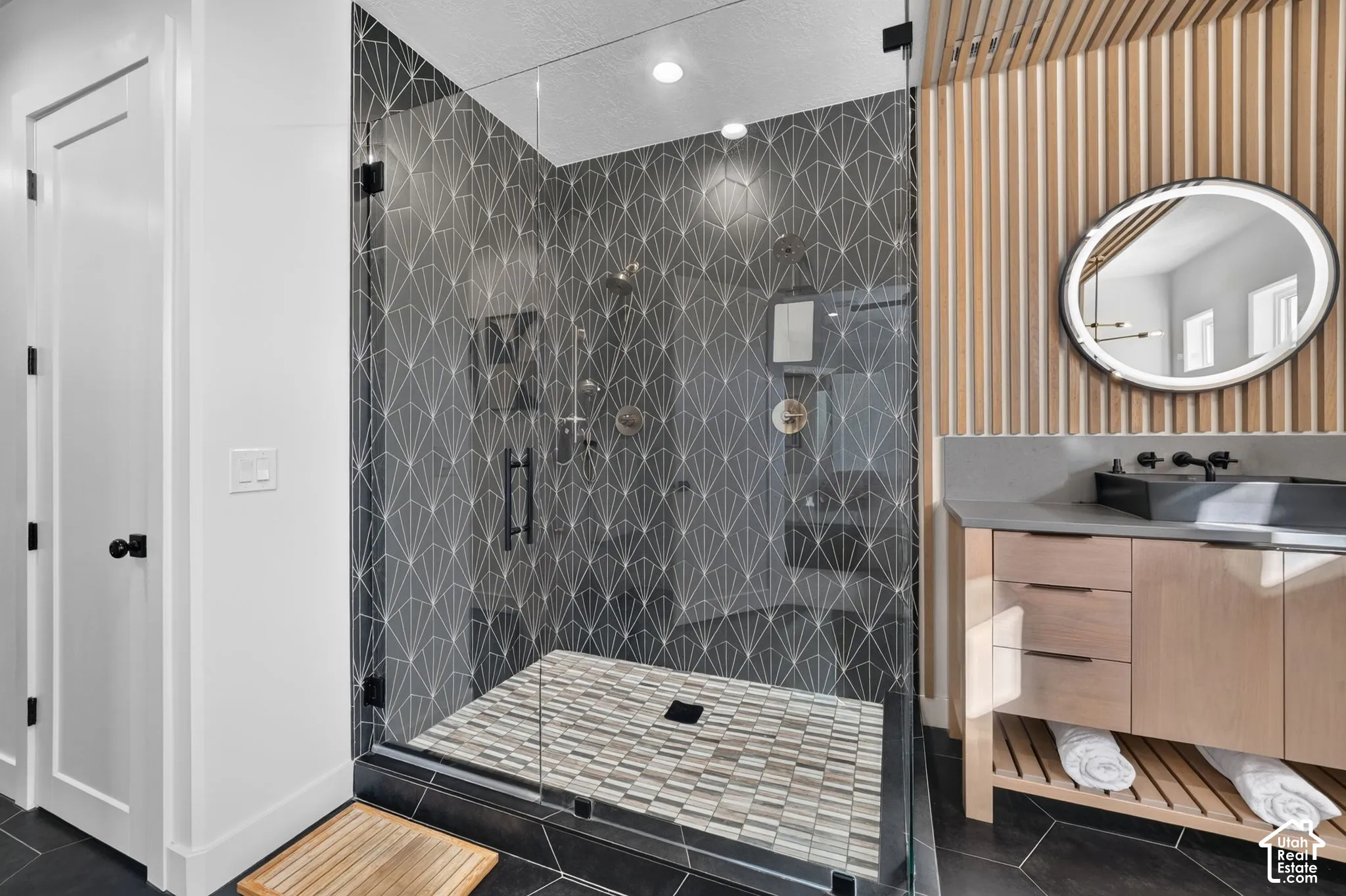 Glass-enclosed shower with patterned tile surround and mosaic floor