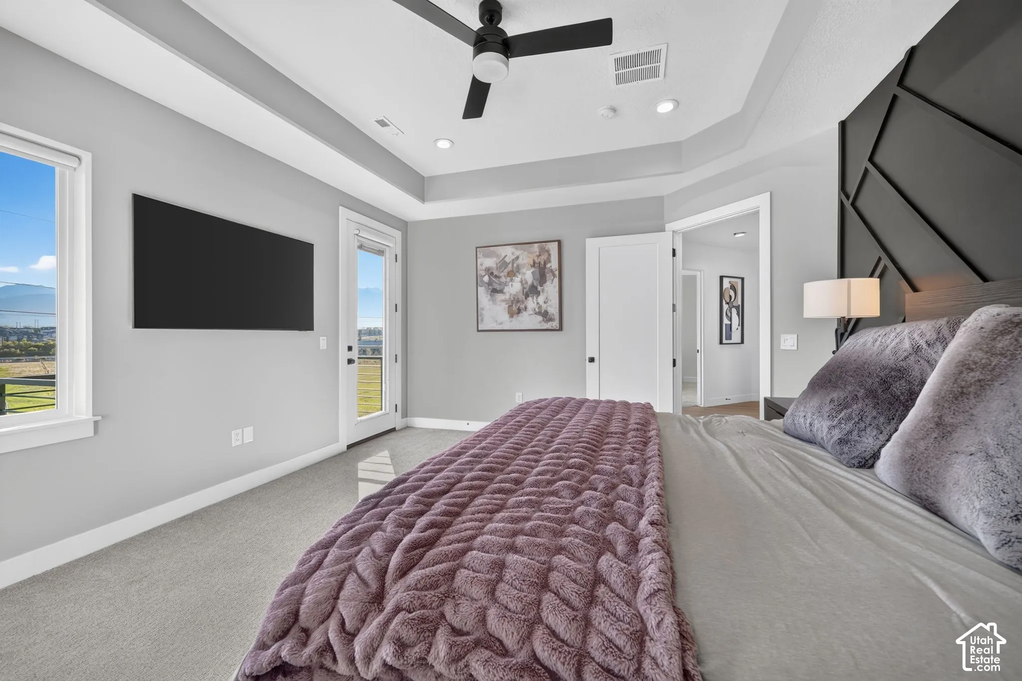 Tray ceiling, recessed lighting, ceiling fan, carpet flooring, and a glass-paneled door