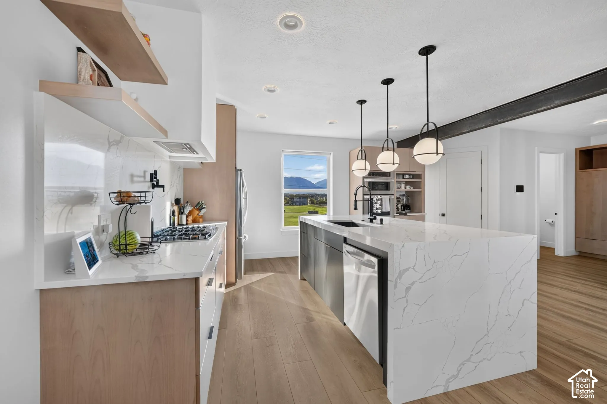 Modern kitchen featuring a large waterfall island with integrated sink, stainless steel appliances, open shelving, and wood-finish flooring