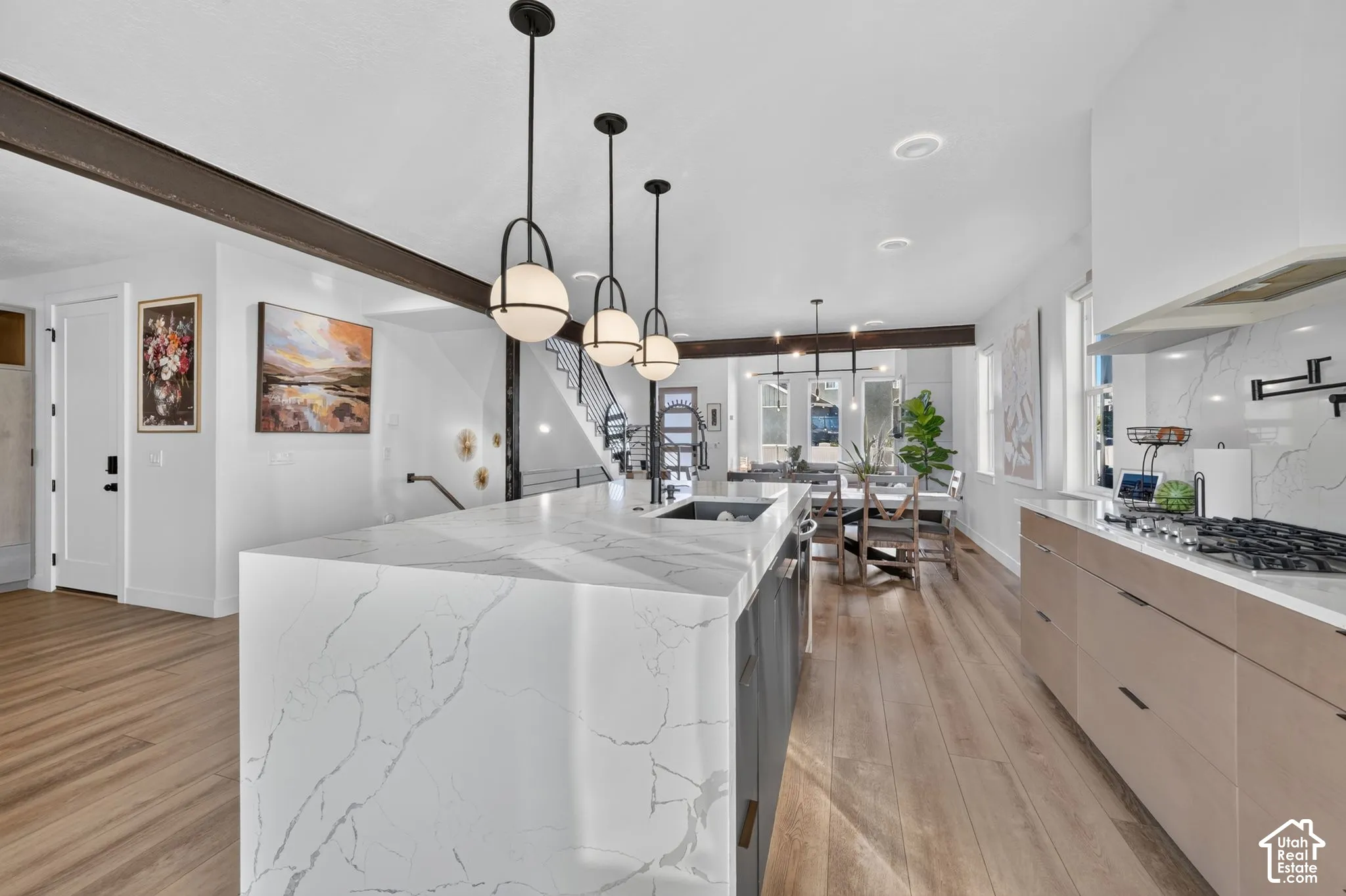 Waterfall-edge island with integrated sink, wood-finish flooring, exposed structural beam, contemporary pendant lighting, and a stainless steel range with a wall-mounted pot filler